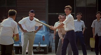 Movie still from “Good Morning, Vietnam” (1987), directed by Barry Levinson – A group of men are playing a game with a baseball bat; Medium shot, Over the shoulder angle