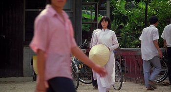 Movie still from “Good Morning, Vietnam” (1987), directed by Barry Levinson – A woman in a long white dress is holding an umbrella; Wide shot, Over the shoulder angle