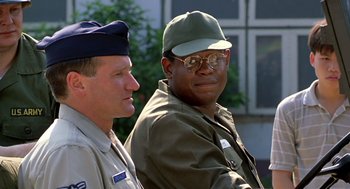 Movie still from “Good Morning, Vietnam” (1987), directed by Barry Levinson – A man in a hat and glasses sitting next to another man in a uniform; Close Up shot, Low angle