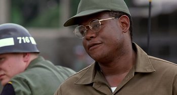 Movie still from “Good Morning, Vietnam” (1987), directed by Barry Levinson – A person wearing glasses and a hat; Close Up shot, Low angle