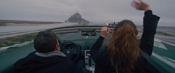 Movie still from “To the Wonder” (2012), directed by Terrence Malick – Two people in a car on a road near a body of water; Wide shot, Low angle