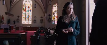 Movie still from “To the Wonder” (2012), directed by Terrence Malick – A woman standing in front of a row of pews holding a cell phone; Medium shot, Low angle