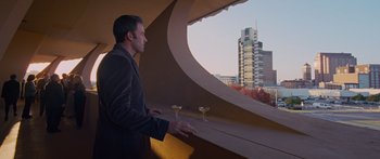 Movie still from “To the Wonder” (2012), directed by Terrence Malick – A man standing next to a window looking out at a city skyline; Wide shot, Low angle