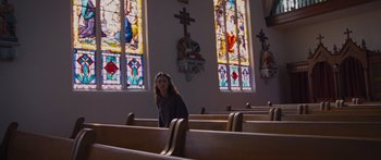 Movie still from “To the Wonder” (2012), directed by Terrence Malick – A woman is sitting in a pew in front of stained - glass windows; Wide shot, Low angle