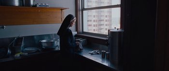Movie still from “To the Wonder” (2012), directed by Terrence Malick – A nun is sitting at a kitchen counter looking out a window; Medium shot, Low angle