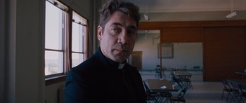 Movie still from “To the Wonder” (2012), directed by Terrence Malick – A man wearing a priest's collar in a room; Close Up shot, Low angle