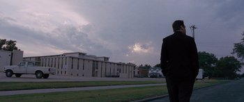 Movie still from “To the Wonder” (2012), directed by Terrence Malick – A man standing on the side of the road in front of a building; Extreme Wide shot, Low angle