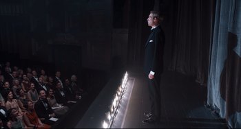Movie still from “Goodbye Christopher Robin” (2017), directed by Simon Curtis – A man standing on a stage in front of candles; Wide shot, High angle