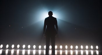 Movie still from “Goodbye Christopher Robin” (2017), directed by Simon Curtis – A man standing in front of a row of light bulbs; Wide shot, Low angle
