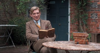 Movie still from “Goodbye Christopher Robin” (2017), directed by Simon Curtis – A man sitting at a table holding an open book; Medium shot, Over the shoulder angle