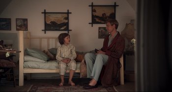 Movie still from “Goodbye Christopher Robin” (2017), directed by Simon Curtis – A man and a boy sitting on a bed in a room; Wide shot, High angle