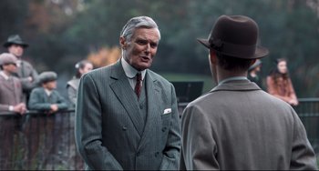 Movie still from “Goodbye Christopher Robin” (2017), directed by Simon Curtis – A man wearing a suit and tie talking to another man; Medium shot, Over the shoulder angle