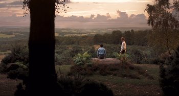 Movie still from “Goodbye Christopher Robin” (2017), directed by Simon Curtis – Two people sitting on a rock in the middle of a field; Extreme Wide shot, High angle