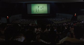 Movie still from “Goodbye, Dragon Inn” (2003), directed by Tsai Ming-liang – People are sitting in a large auditorium watching a movie; Extreme Wide shot, High angle