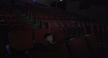 Movie still from “Goodbye, Dragon Inn” (2003), directed by Tsai Ming-liang – A little boy sitting in a chair in a theater; Wide shot, High angle
