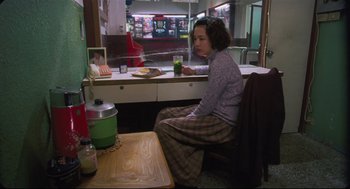 Movie still from “Goodbye, Dragon Inn” (2003), directed by Tsai Ming-liang – A woman sitting at a table with a glass of juice; Medium shot, High angle
