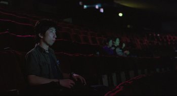 Movie still from “Goodbye, Dragon Inn” (2003), directed by Tsai Ming-liang – A man sitting in a theater holding a game controller; Medium shot, High angle