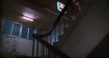 Movie still from “Goodbye, Dragon Inn” (2003), directed by Tsai Ming-liang – A view of a staircase with a sign on the wall; Wide shot, Low angle
