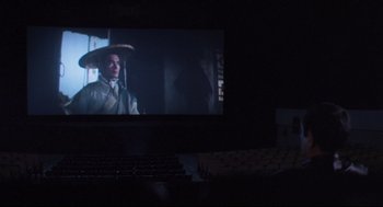 Movie still from “Goodbye, Dragon Inn” (2003), directed by Tsai Ming-liang – A movie screen with a man wearing a hat on top of it; Wide shot, High angle