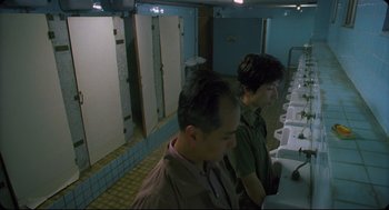 Movie still from “Goodbye, Dragon Inn” (2003), directed by Tsai Ming-liang – Two men are standing in a bathroom looking in the mirror; Medium shot, Low angle