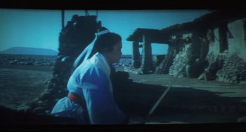 Movie still from “Goodbye, Dragon Inn” (2003), directed by Tsai Ming-liang – A man sitting on the ground in front of a building; Wide shot, High angle