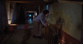 Movie still from “Goodbye, Dragon Inn” (2003), directed by Tsai Ming-liang – An older woman is cleaning a stair railing in an old house; Wide shot, High angle
