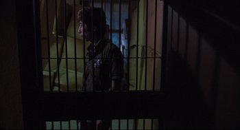 Movie still from “Goodbye, Dragon Inn” (2003), directed by Tsai Ming-liang – A man standing behind bars in a jail cell; Medium shot, Low angle
