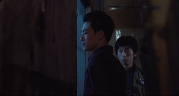 Movie still from “Goodbye, Dragon Inn” (2003), directed by Tsai Ming-liang – Two young men standing next to each other in a dark room; Medium shot, Over the shoulder angle