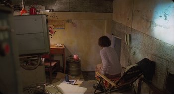 Movie still from “Goodbye, Dragon Inn” (2003), directed by Tsai Ming-liang – A woman sitting on a chair in a room; Wide shot, High angle