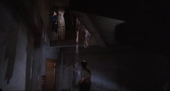 Movie still from “Goodbye, Dragon Inn” (2003), directed by Tsai Ming-liang – A man standing in a dark room next to a staircase; Wide shot, Low angle