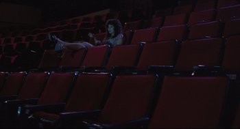 Movie still from “Goodbye, Dragon Inn” (2003), directed by Tsai Ming-liang – A woman sitting in a red chair in an empty theater; Extreme Wide shot, High angle