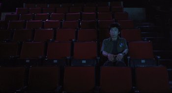 Movie still from “Goodbye, Dragon Inn” (2003), directed by Tsai Ming-liang – A man sitting in a red chair in an empty theater; Wide shot, High angle