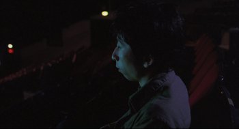 Movie still from “Goodbye, Dragon Inn” (2003), directed by Tsai Ming-liang – A man is standing in the dark in front of a projector; Close Up shot, Low angle