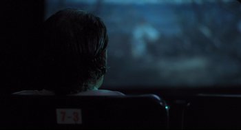 Movie still from “Goodbye, Dragon Inn” (2003), directed by Tsai Ming-liang – A woman sitting in front of a tv in a dark room; Close Up shot, Over the shoulder angle