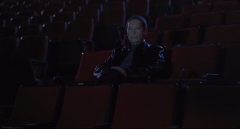 Movie still from “Goodbye, Dragon Inn” (2003), directed by Tsai Ming-liang – A man sitting in a movie theater with his arms crossed; Wide shot, High angle