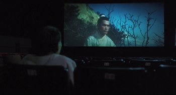 Movie still from “Goodbye, Dragon Inn” (2003), directed by Tsai Ming-liang – A person sitting in front of a television screen; Wide shot, Over the shoulder angle