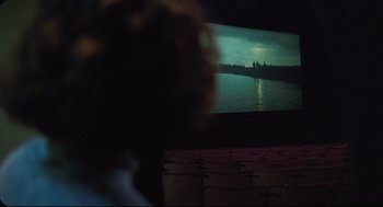 Movie still from “Goodbye, Dragon Inn” (2003), directed by Tsai Ming-liang – A person is watching a movie on a projector screen; Extreme Wide shot, Over the shoulder angle