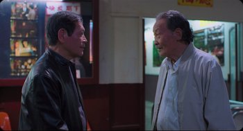 Movie still from “Goodbye, Dragon Inn” (2003), directed by Tsai Ming-liang – Two older men talking to each other in front of a window; Medium shot, Over the shoulder angle