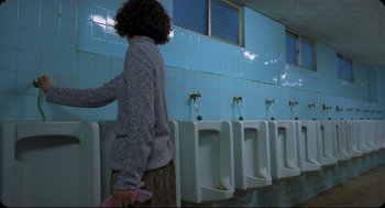 Movie still from “Goodbye, Dragon Inn” (2003), directed by Tsai Ming-liang – A woman standing in front of urinals in a bathroom; Medium shot, Low angle