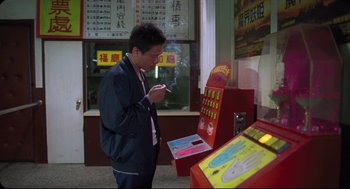 Movie still from “Goodbye, Dragon Inn” (2003), directed by Tsai Ming-liang – A man smoking a cigarette in front of an advertisement; Medium shot, High angle