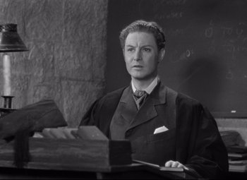 Movie still from “Goodbye, Mr. Chips” (1939), directed by Sam Wood – A man wearing a suit and tie sitting at a desk; Medium shot, High angle