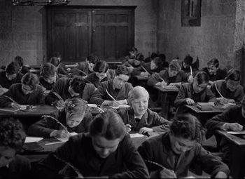 Movie still from “Goodbye, Mr. Chips” (1939), directed by Sam Wood – A group of people sitting at a table writing on papers; Medium shot, High angle