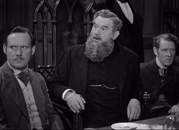 Movie still from “Goodbye, Mr. Chips” (1939), directed by Sam Wood – A man sitting at a table with two other men; Medium shot, Over the shoulder angle