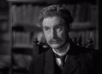 Movie still from “Goodbye, Mr. Chips” (1939), directed by Sam Wood – A man in a suit standing in front of a bookshelf; Close Up shot, Over the shoulder angle