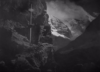 Movie still from “Goodbye, Mr. Chips” (1939), directed by Sam Wood – A man standing next to a cross on top of a mountain; Wide shot, High angle