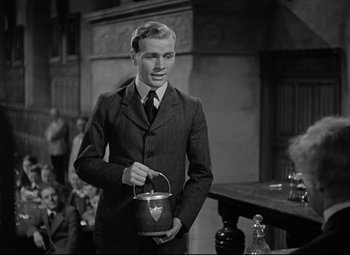 Movie still from “Goodbye, Mr. Chips” (1939), directed by Sam Wood – A man in a suit and tie holding a bucket; Medium shot, Low angle