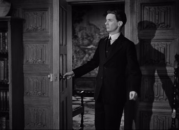 Movie still from “Goodbye, Mr. Chips” (1939), directed by Sam Wood – A black and white photo of a man in a suit opening a door; Medium shot, Low angle