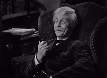 Movie still from “Goodbye, Mr. Chips” (1939), directed by Sam Wood – An older man sitting in a chair holding a pair of glasses; Close Up shot, High angle