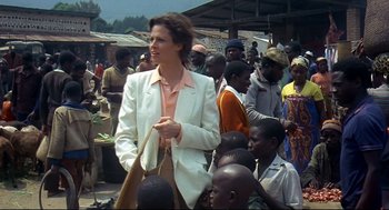 Movie still from “Gorillas in the Mist” (1988), directed by Michael Apted – A woman in a white jacket is holding a brown bag; Medium shot, Over the shoulder angle