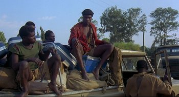 Movie still from “Gorillas in the Mist” (1988), directed by Michael Apted – A man sitting on the back of a pick - up truck; Medium shot, Low angle